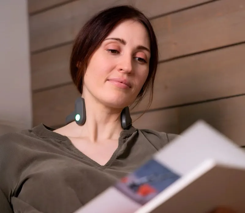 Mujer leyendo un libro por la noche con el dispositivo Pulsetto en el cuello